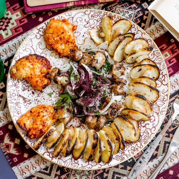 A large platter of Lebanese grilled chicken, meat, onions, and roasted potatoes on a patterned tablecloth.