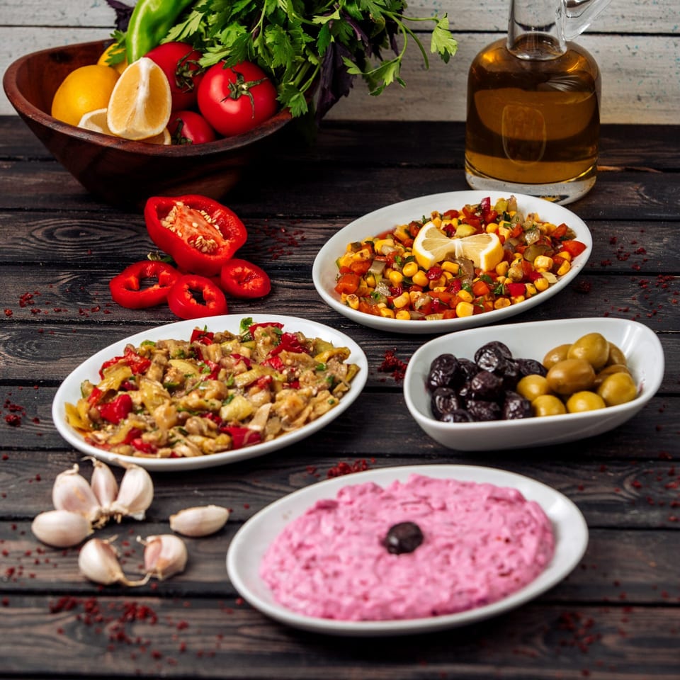 A spread of Lebanese mezze, including salads, olives, and a pink dip, with fresh vegetables.