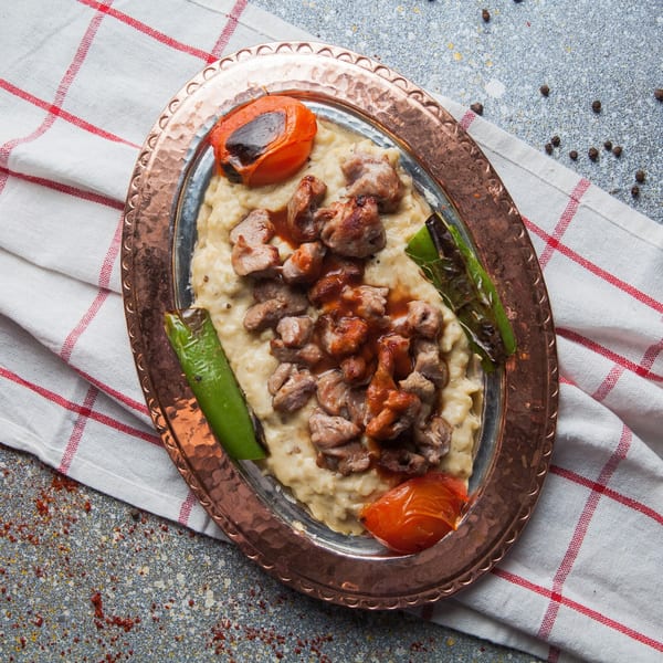 Kamal's Kafe's Lebanese dish with meat, sauce, roasted tomatoes, and green peppers on a copper platter.