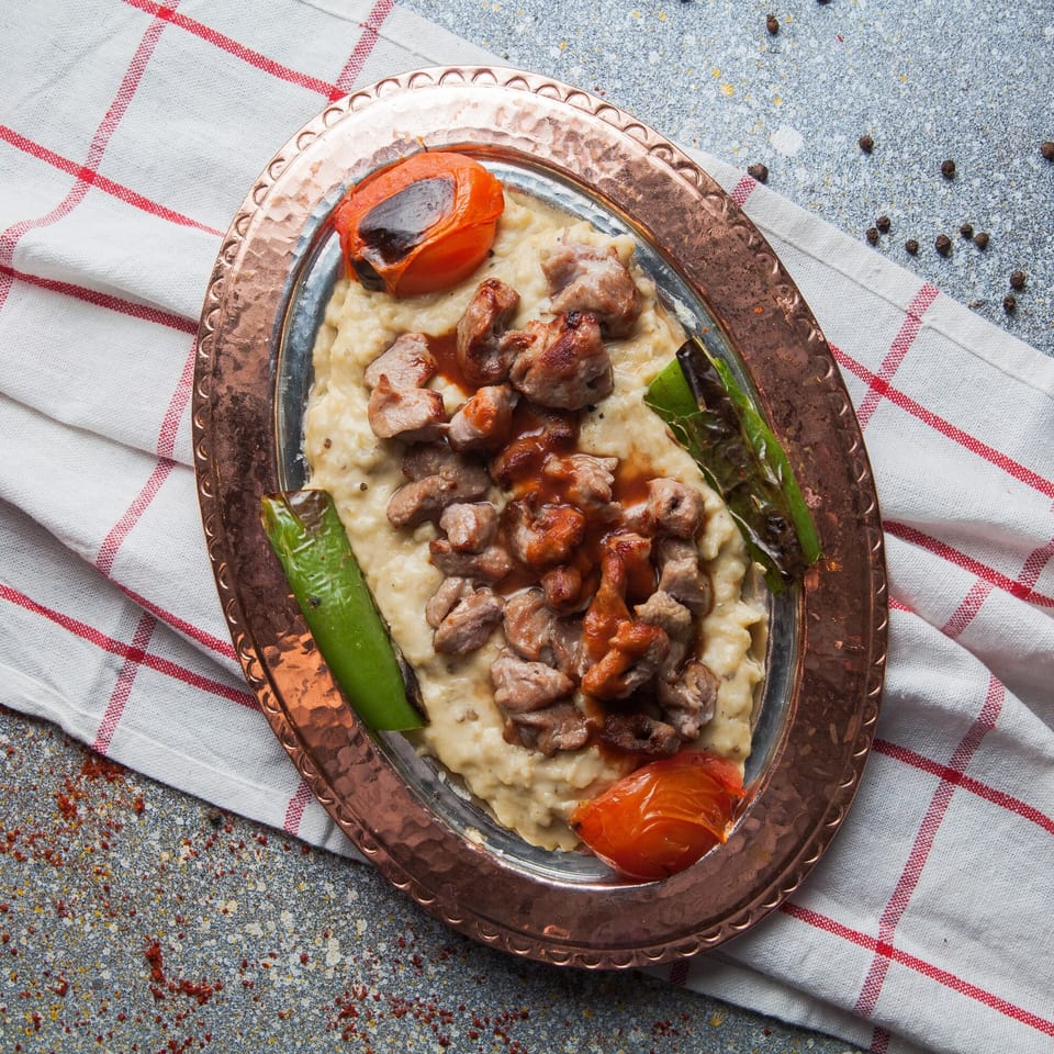 Kamal's Kafe's Lebanese dish with meat, sauce, roasted tomatoes, and green peppers on a copper platter.