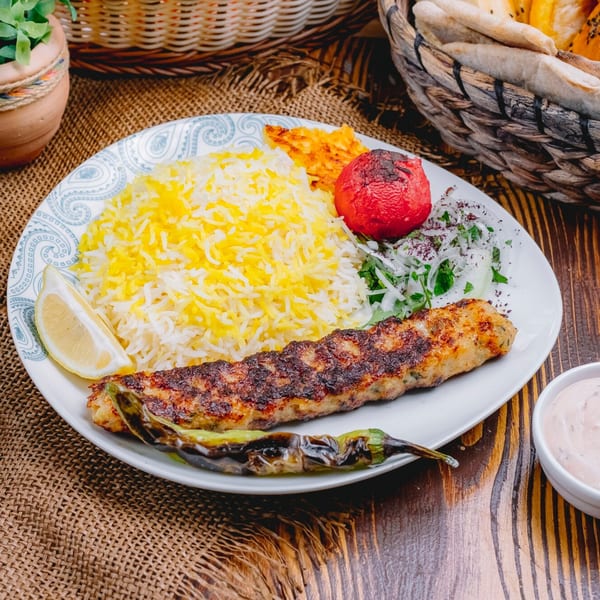 Kamal's Kafe's Lebanese kofta kebab with rice, grilled tomato, onion salad, and lemon wedge.