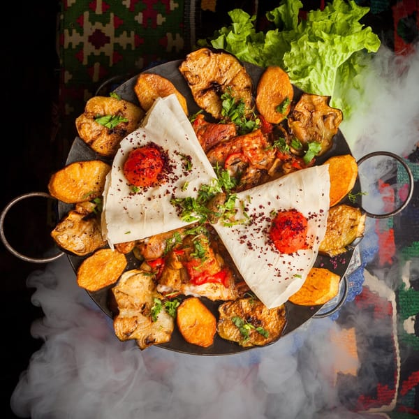 Lebanese platter with grilled vegetables, flatbread, and red sauce, surrounded by smoke.